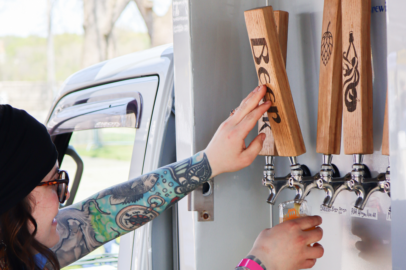 Person with tattoos using a tap at a mobile beer station.
